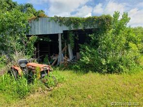 An old tractor sits in front of a weathered metal shed overgrown with vegetation — 618 INGHAM ROAD, NEW SMYRNA BEACH, FL