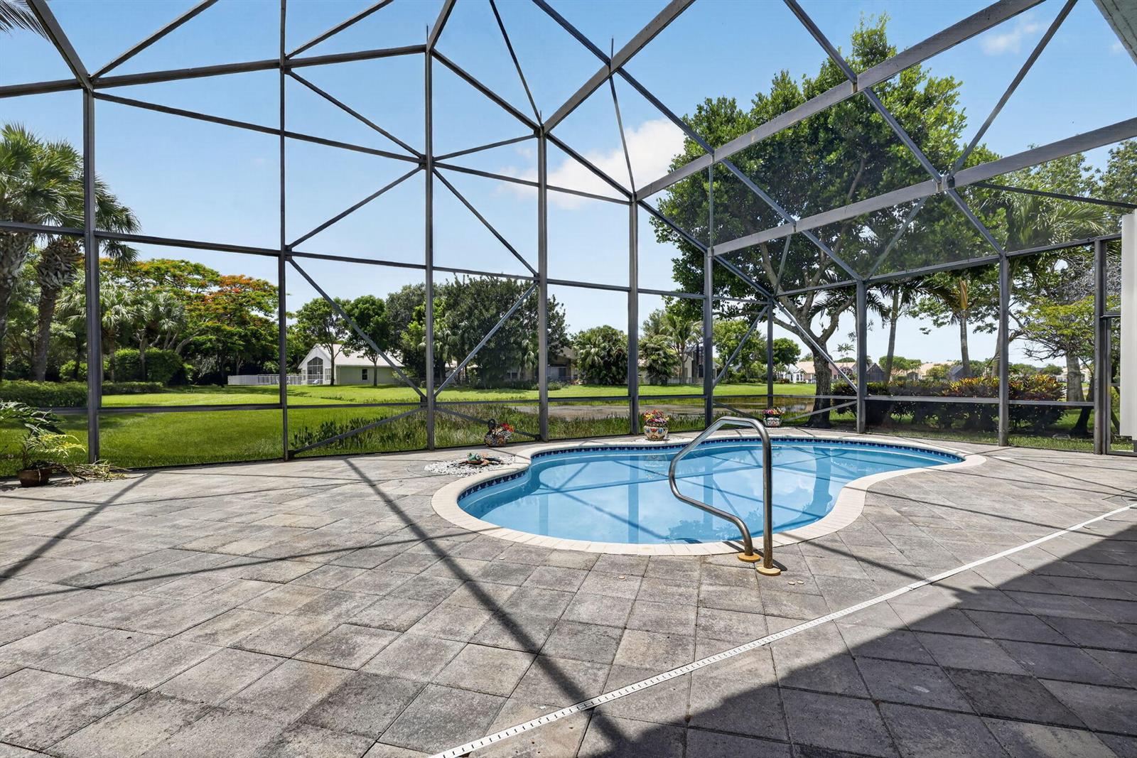 A screened-in patio features a kidney-shaped swimming pool and stone pavers overlooking a grassy yard — 6550 Sand City Way, Delray Beach FL 33446, DELRAY BEACH, FL