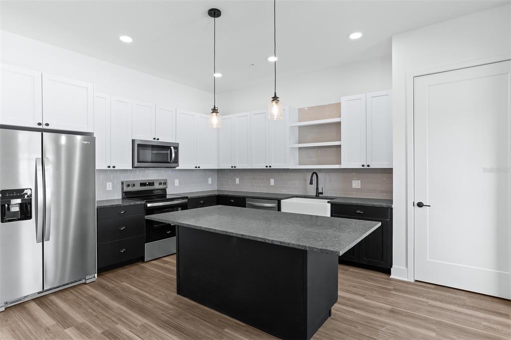 A modern kitchen features white upper cabinets, dark lower cabinets, a gray island, and stainless appliances — 3814 FERN HOLLOW PLACE, TAMPA, FL