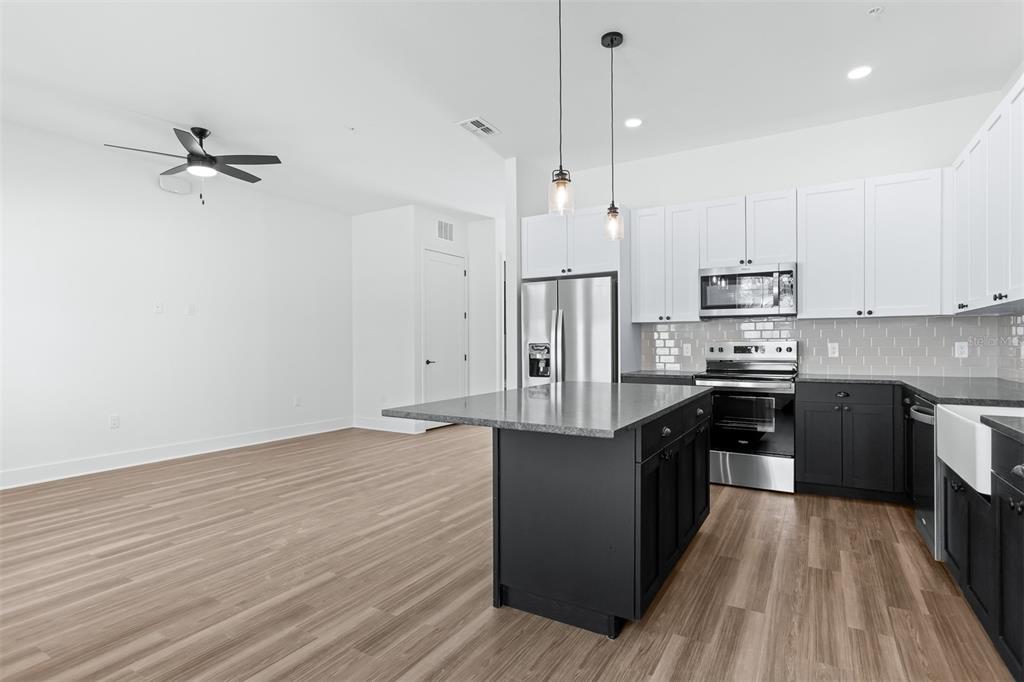 A modern kitchen features a dark island, white upper cabinets, and stainless steel appliances — 3814 FERN HOLLOW PLACE, TAMPA, FL