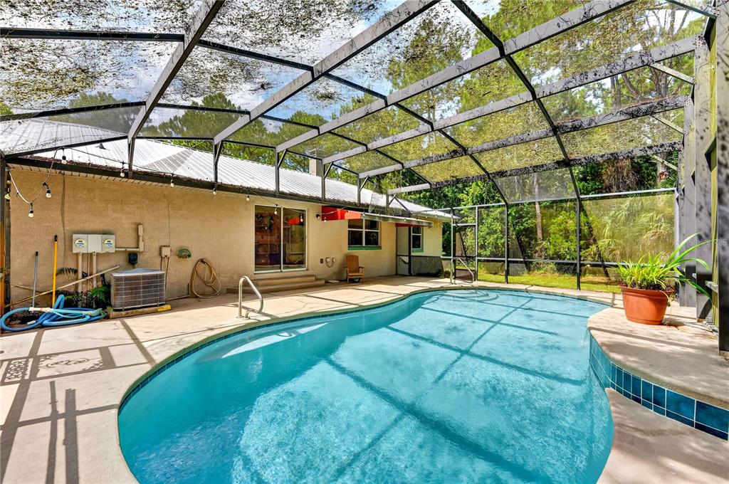 A swimming pool sits inside a screened-in patio area next to a tan stucco house — 590 COUNTY ROAD 325, BUNNELL, FL