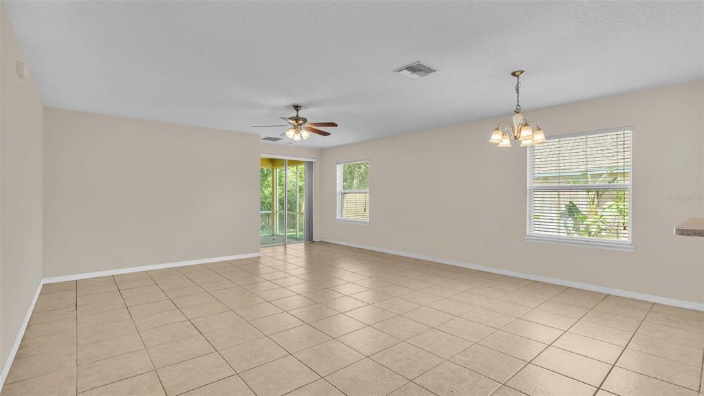 An empty living and dining area with beige tile floors, a ceiling fan, and windows — 6838 GLENBROOK DRIVE, LAKELAND, FL