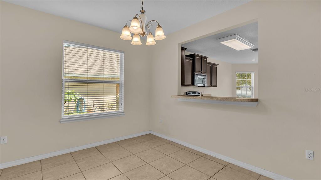 A dining area with tile flooring, a chandelier, and a pass-through window to the kitchen — 6838 GLENBROOK DRIVE, LAKELAND, FL