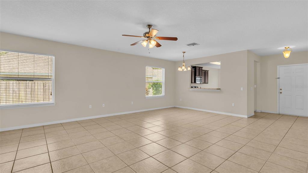 A spacious living room features beige tile flooring, neutral walls, a ceiling fan, and windows — 6838 GLENBROOK DRIVE, LAKELAND, FL