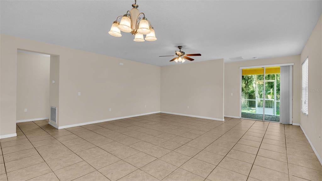 An empty living room features beige walls, tile flooring, a ceiling fan, and sliding doors — 6838 GLENBROOK DRIVE, LAKELAND, FL