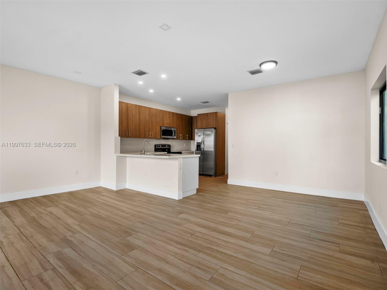 An open-concept kitchen features wood-grain cabinets, stainless steel appliances, and light-colored wood flooring — 5428 NW 3rd Ave, Miami FL 33127, MIAMI, FL