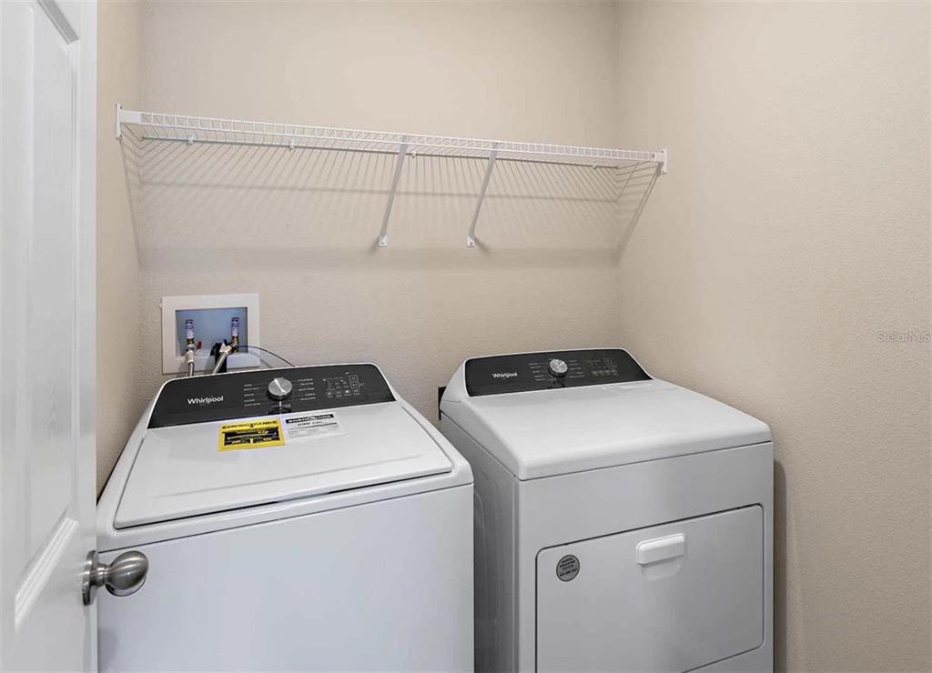 A laundry room features a white washer and dryer beneath a wire storage shelf — 12935 HAWKSTONE TRAIL BOULEVARD, LITHIA, FL