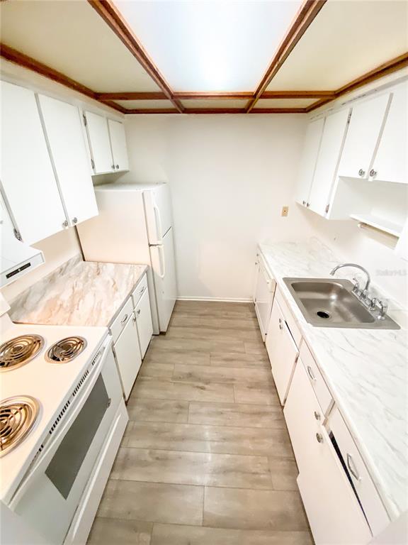 A galley kitchen features white cabinets, marble-patterned countertops, stainless steel appliances, and wood-look flooring — 4325 AEGEAN DRIVE UNIT 128B, TAMPA, FL