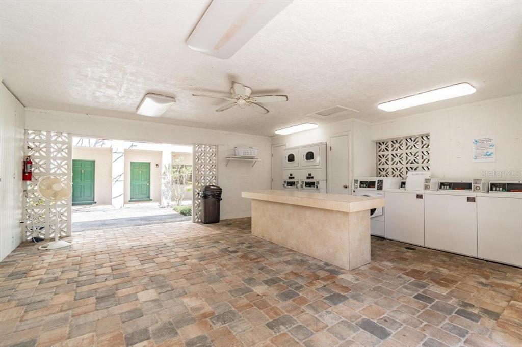 A laundry room with brick flooring, a central counter, and multiple washers and dryers — 4325 AEGEAN DRIVE UNIT 128B, TAMPA, FL