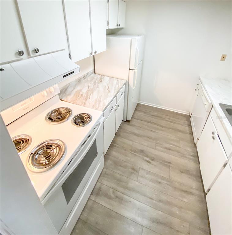 A kitchen features white cabinets, white appliances, marble-patterned countertops, and light wood-look flooring — 4325 AEGEAN DRIVE UNIT 128B, TAMPA, FL