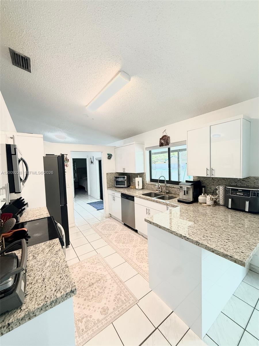 A kitchen features white cabinets, granite countertops, stainless steel appliances, and white tile flooring — 11216 SW 166th Ter, Miami FL 33157, MIAMI, FL