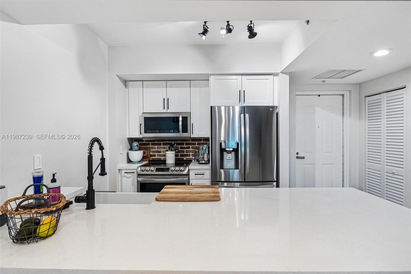 A kitchen features white cabinets, stainless steel appliances, a brick backsplash, and a white island — 7290 SW 90th St # 202, Miami FL 33156, MIAMI, FL