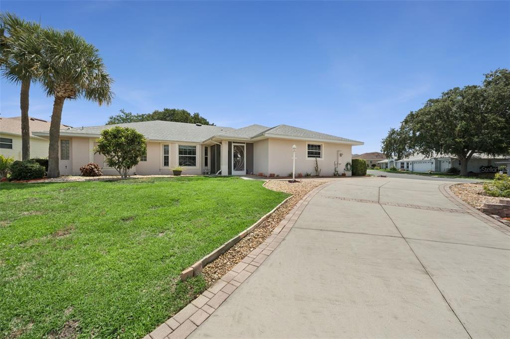A single-story house with a beige exterior, a concrete driveway, and palm trees — 21101 BRAVEHEART DRIVE, LEESBURG, FL