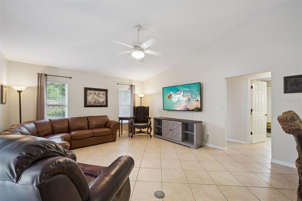 A living room features a leather sectional, a wall-mounted television, and light-colored tile flooring — 21101 BRAVEHEART DRIVE, LEESBURG, FL