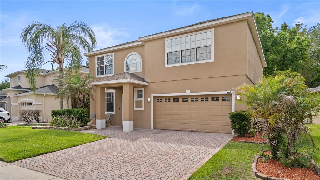 A two-story tan house with a paved driveway, a two-car garage, and palm trees — 2908 DAYBREAK DRIVE, ORLANDO, FL