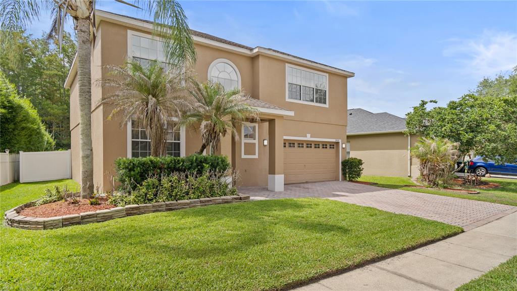 A two-story tan stucco house with a paved driveway, a front lawn, and palm trees — 2908 DAYBREAK DRIVE, ORLANDO, FL