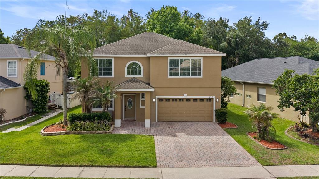 A two-story tan house with a brick driveway, a palm tree, and a two-car garage — 2908 DAYBREAK DRIVE, ORLANDO, FL