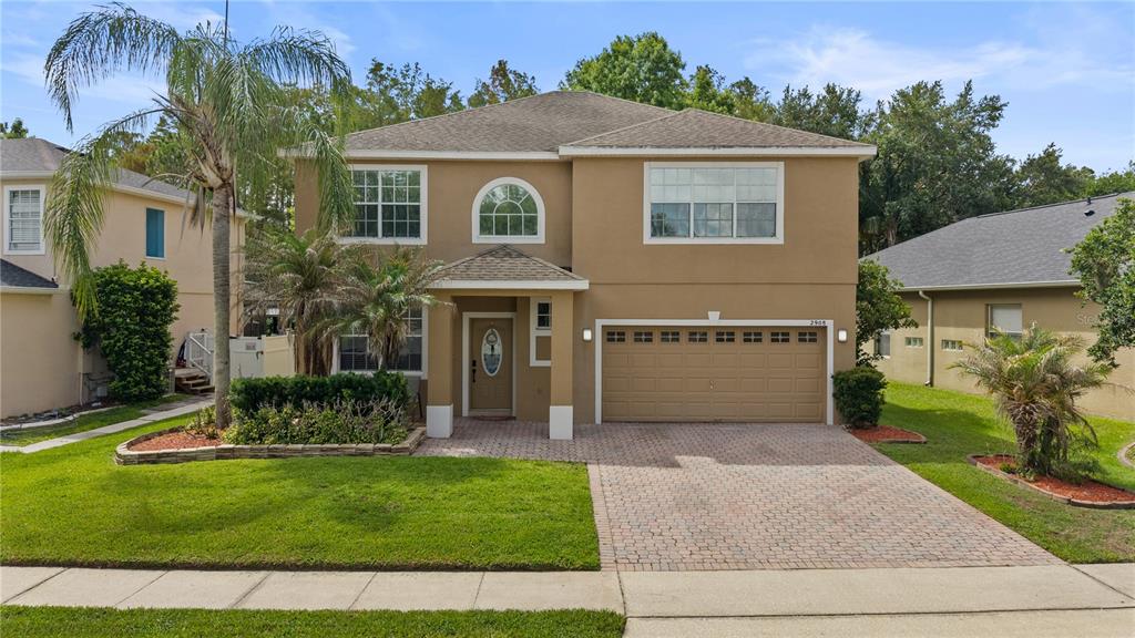 A two-story tan stucco house features a paved driveway, a two-car garage, and landscaping — 2908 DAYBREAK DRIVE, ORLANDO, FL