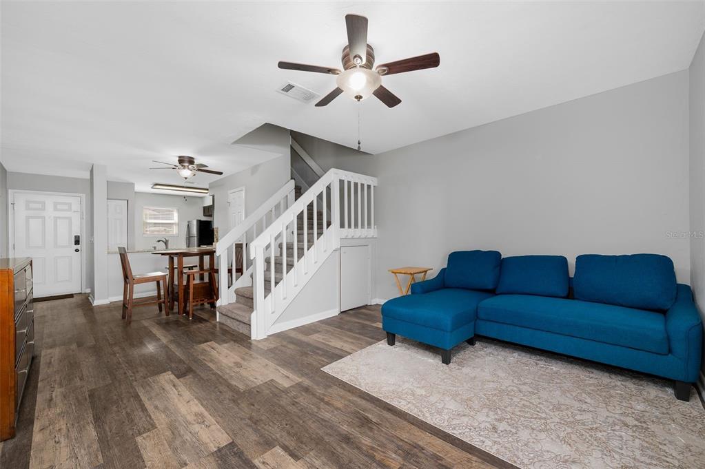A living room with wood-look flooring, a blue sectional sofa, and stairs leading upstairs — 2132 SW 39TH DRIVE, GAINESVILLE, FL