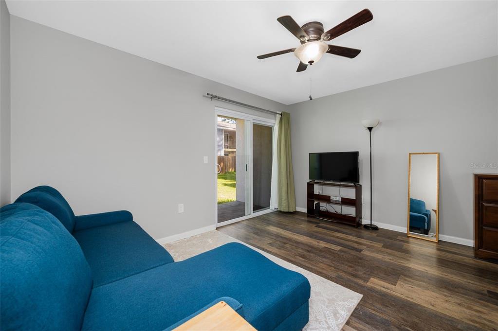 A living room features a blue sectional sofa, wood-look flooring, a ceiling fan, and sliding doors — 2132 SW 39TH DRIVE, GAINESVILLE, FL