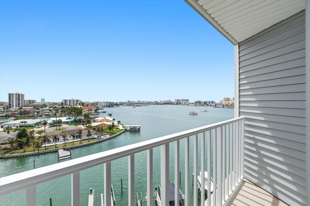 A balcony with a white railing overlooks a bay with boats and coastal buildings — 610 ISLAND WAY UNIT 607, CLEARWATER BEACH, FL