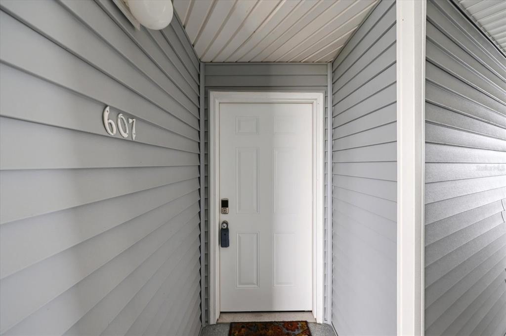 A white front door with a smart lock is set within a gray vinyl-sided entryway — 610 ISLAND WAY UNIT 607, CLEARWATER BEACH, FL