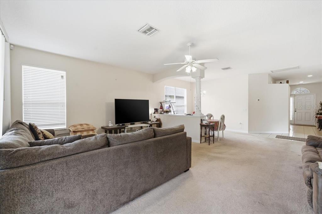 A living room with beige carpet, a gray sectional sofa, and an open dining area — 18425 CYPRESS BAY PARKWAY, LAND O LAKES, FL