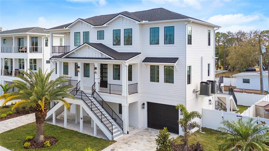 A white, elevated two-story house with a black roof, front staircase, and ground-level garage — 220 90TH AVENUE NE, ST PETERSBURG, FL