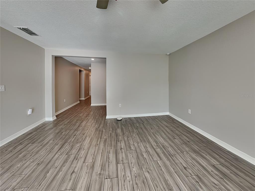 An empty room with gray walls and wood-look flooring leads into a hallway — 304 KENSINGTON VIEW DRIVE, WINTER HAVEN, FL
