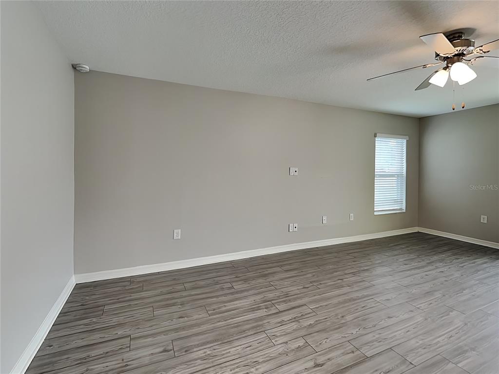 An empty room features gray walls, wood-look flooring, a ceiling fan, and a window — 304 KENSINGTON VIEW DRIVE, WINTER HAVEN, FL