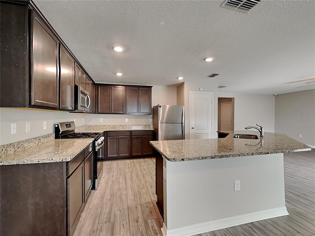 A kitchen features dark wood cabinets, granite countertops, stainless steel appliances, and wood-look flooring — 304 KENSINGTON VIEW DRIVE, WINTER HAVEN, FL