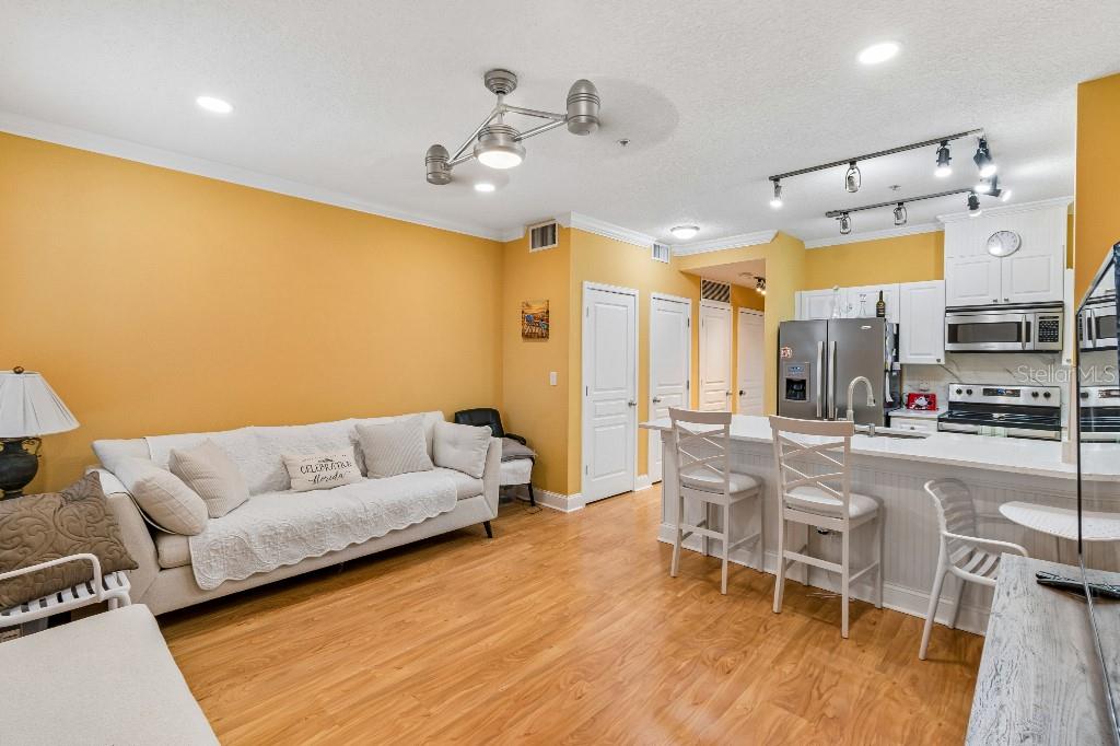 A living room with yellow walls and hardwood floors opens into a white kitchen area — 600 MARKET STREET UNIT 230, CELEBRATION, FL