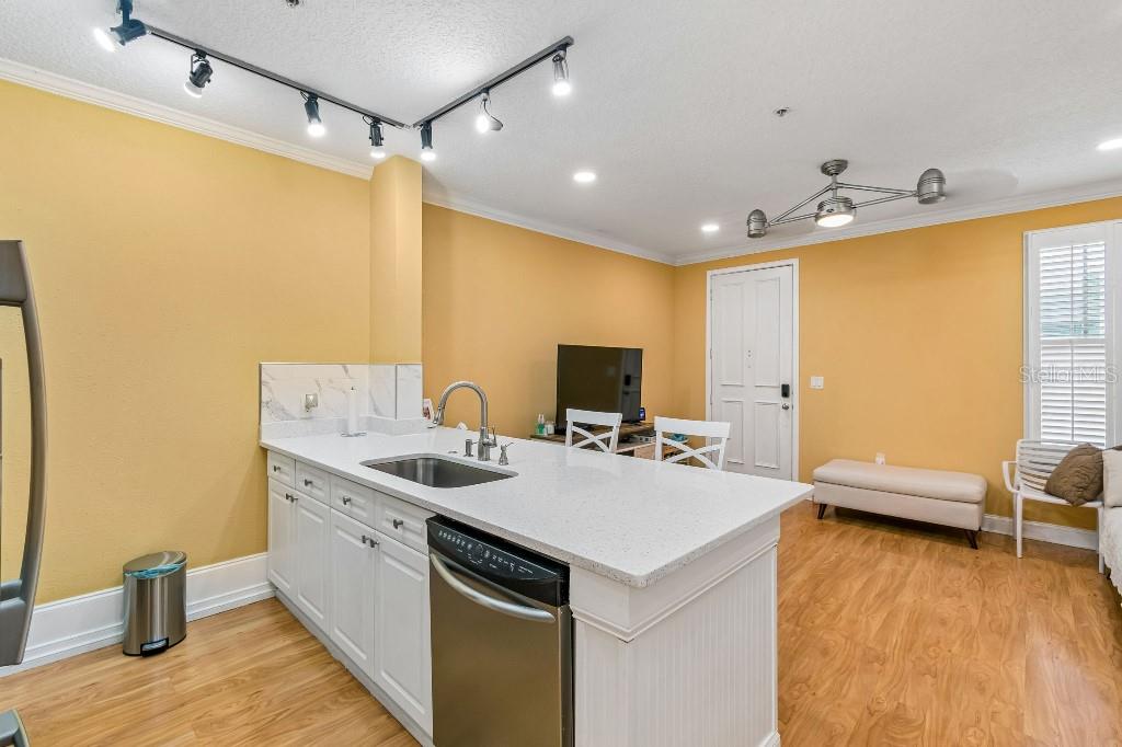 A kitchen island with a stainless steel dishwasher and sink sits before a yellow-walled room — 600 MARKET STREET UNIT 230, CELEBRATION, FL