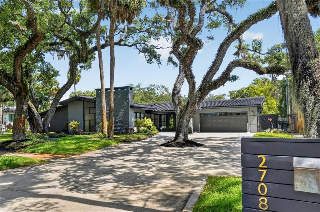 A single-story house with a dark gray exterior, a paved driveway, and large oak trees — 2708 N DUNDEE STREET, TAMPA, FL