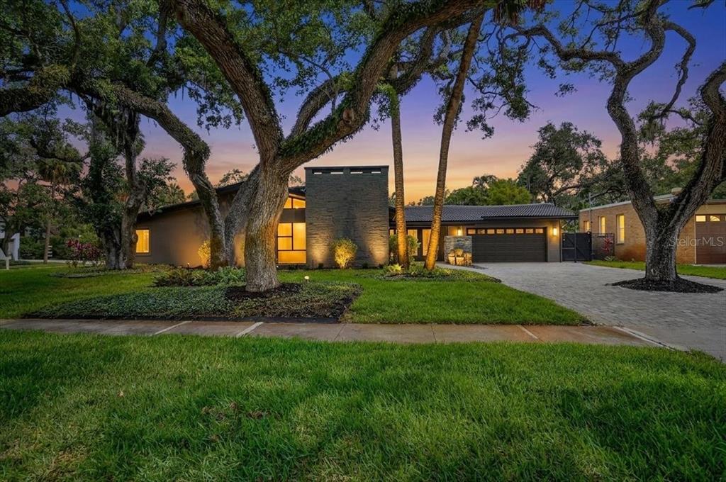 A modern single-story house with a stone chimney and a paved driveway under large trees — 2708 N DUNDEE STREET, TAMPA, FL
