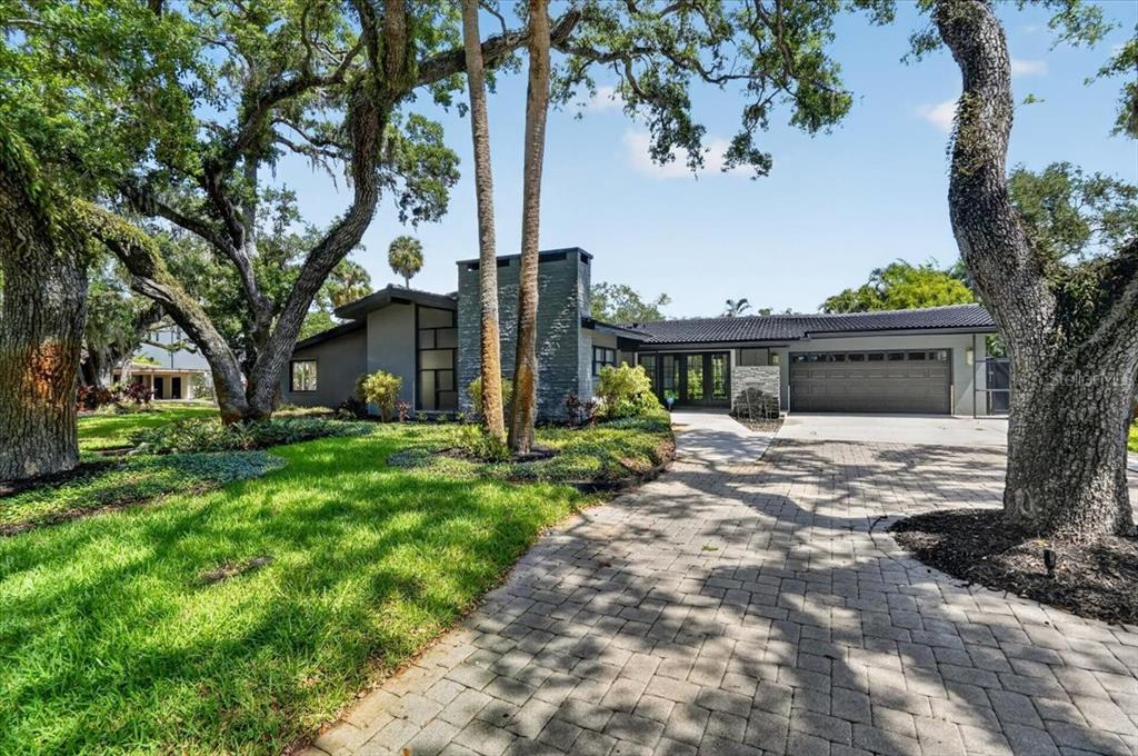 A modern gray house with a stone chimney and a paved driveway under large trees — 2708 N DUNDEE STREET, TAMPA, FL