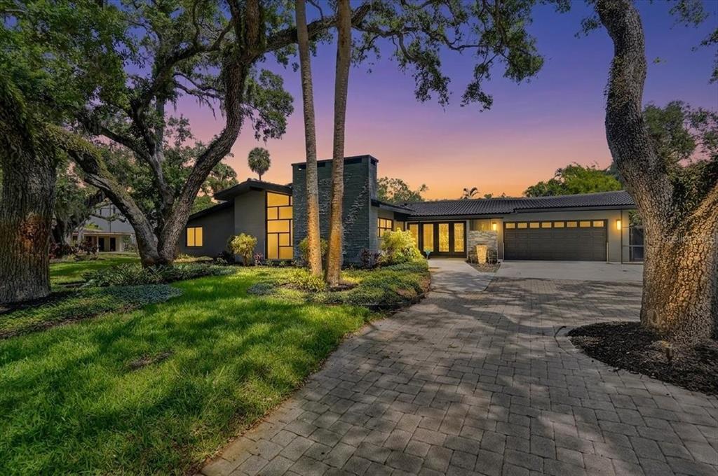 A modern house with a stone chimney, paved driveway, and large trees at sunset — 2708 N DUNDEE STREET, TAMPA, FL