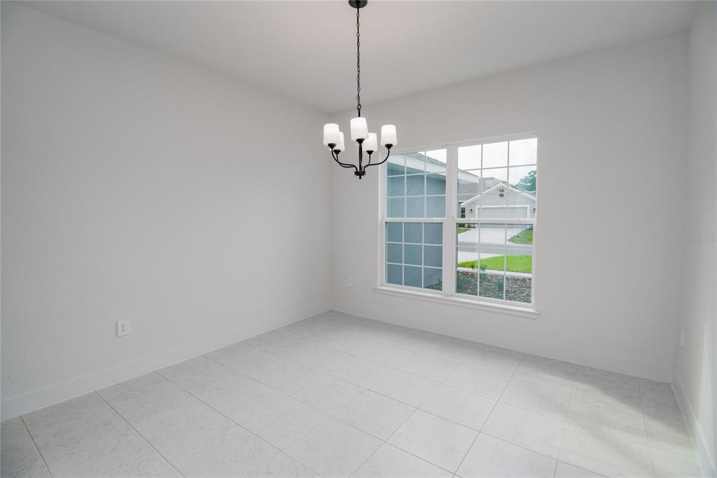 An empty dining room features white walls, light tile flooring, and a black chandelier — 1222 HICKORY NUT DRIVE, LAKE WALES, FL