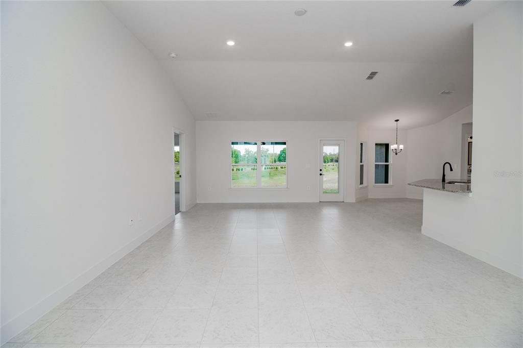A bright, open-concept living area features white walls, light tile flooring, and a kitchen island — 1222 HICKORY NUT DRIVE, LAKE WALES, FL