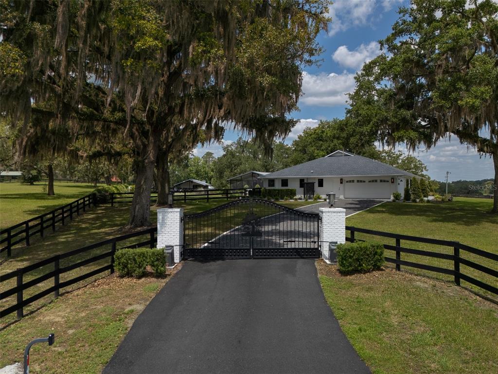 A gated driveway leads to a white house with a dark roof and large trees — 10250 NW 76TH TERRACE, OCALA, FL