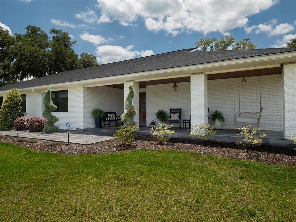 A white brick ranch house features a long covered front porch with a hanging swing — 10250 NW 76TH TERRACE, OCALA, FL