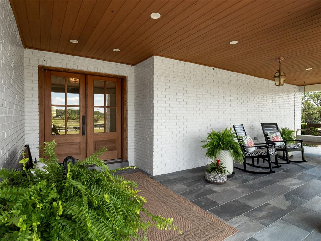 A covered porch features white brick walls, a wood-paneled ceiling, and dark stone flooring — 10250 NW 76TH TERRACE, OCALA, FL
