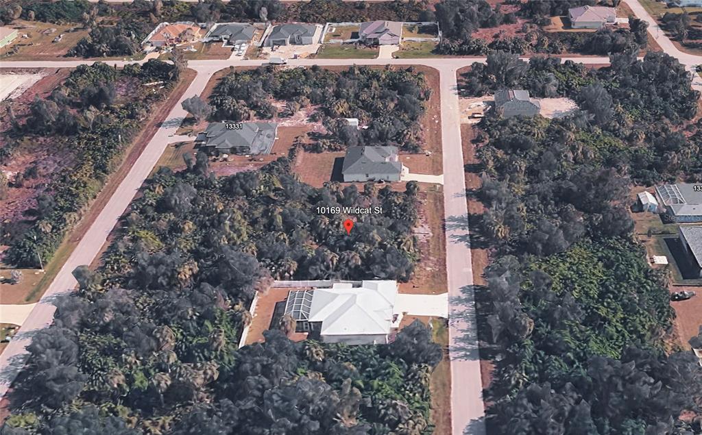 This aerial view shows a residential lot with dense vegetation and nearby houses — 10169 WILDCAT STREET, PORT CHARLOTTE, FL