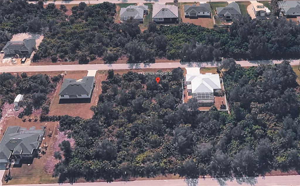 An aerial view shows a vacant, wooded residential lot situated between two existing houses — 10169 WILDCAT STREET, PORT CHARLOTTE, FL