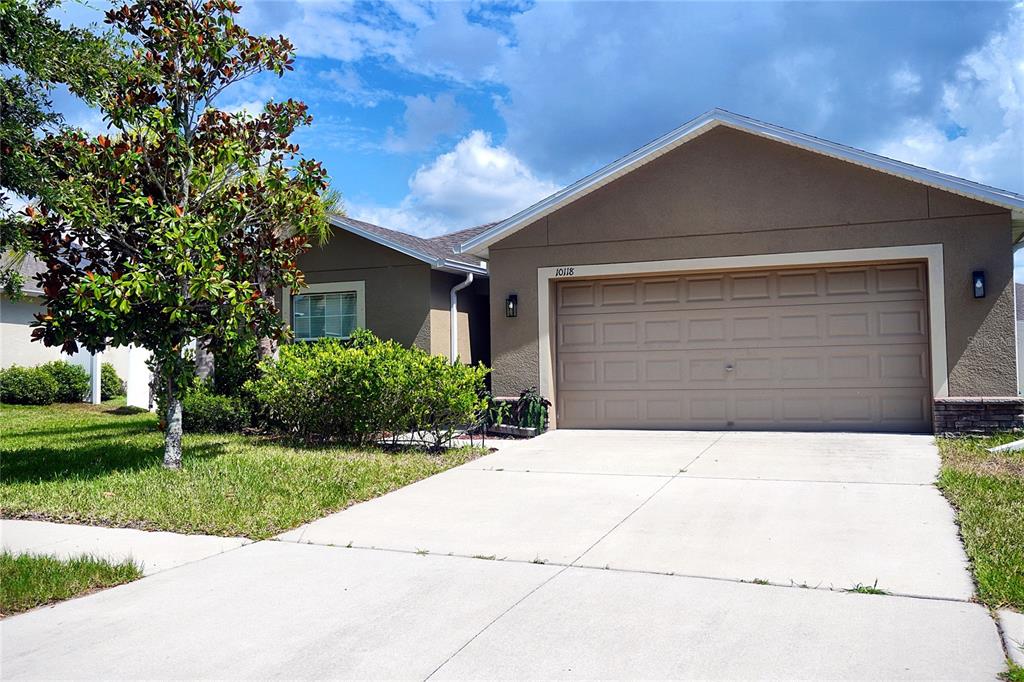 A single-story house with a tan stucco exterior, a two-car garage, and a front lawn — 10118 PENWOOD WAY, HUDSON, FL