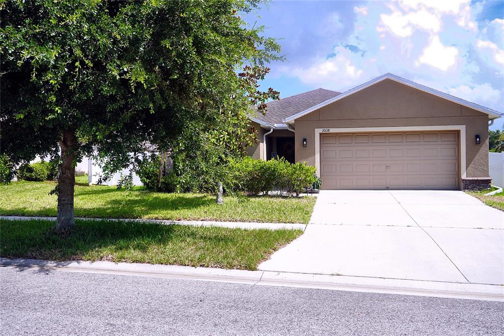 A tan single-story house with a two-car garage and a large tree in the yard — 10118 PENWOOD WAY, HUDSON, FL
