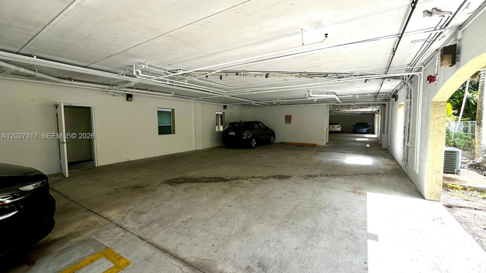 A covered parking garage features concrete floors, white walls, and exposed overhead pipes — 1025 SW 7th Ave # 5, Miami FL 33130, MIAMI, FL