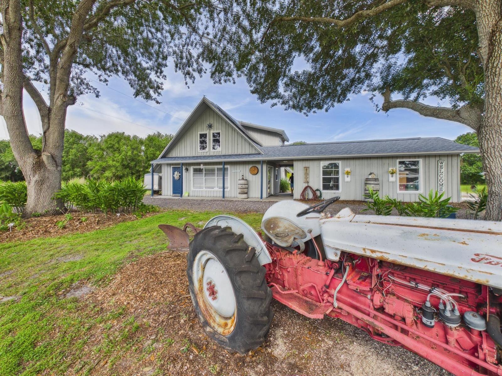 An old red and white tractor sits in front of a gray farmhouse-style building — 136 SW 85th Avenue, Okeechobee FL 34974, OKEECHOBEE, FL