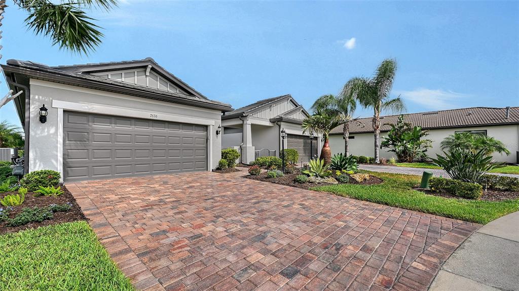 A paved driveway leads to the garage of a single-story house with palm trees — 7636 KIRKLAND COVE, LAKEWOOD RANCH, FL