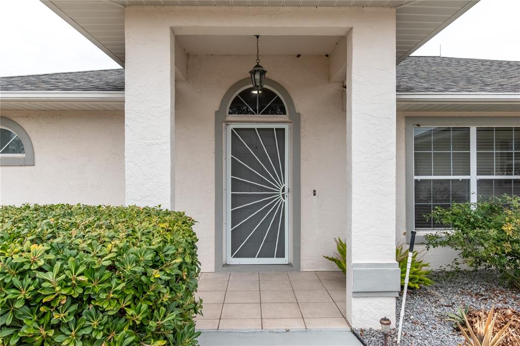 The exterior of a light-colored house features a corner accent wall and a small patio — 5011 NW 31ST STREET, OCALA, FL